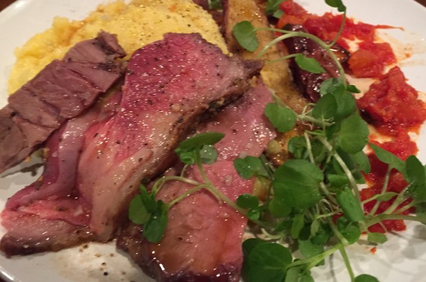Plated leg of lamb with polenta, roasted sweet potatoes and carrots, veal demi-glace, and tomato reduction.  Garnished with watercress.  Notice the three different pieces and their varying levels of doneness.