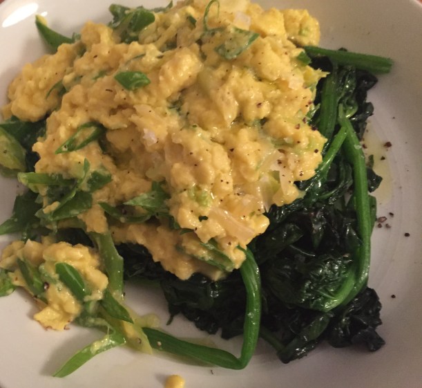 Creamy scrambled eggs over wilted greens is a quick and easy way to have a meal that tastes great and is easy on the budget.